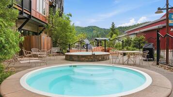 A swimming pool with a stone surround, outdoor seating, and a view of a forested hill.