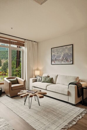 Ein Wohnzimmer mit einer Couch, einem Sessel, einem Couchtisch und einem großen Fenster mit Vorhängen.