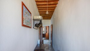 Un couloir étroit avec un sol carrelé, un banc en bois, un ventilateur de plafond et une porte au fond.