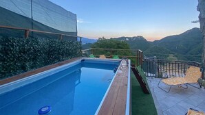 Piscina com deck de madeira, área de estar externa e vista para montanhas.