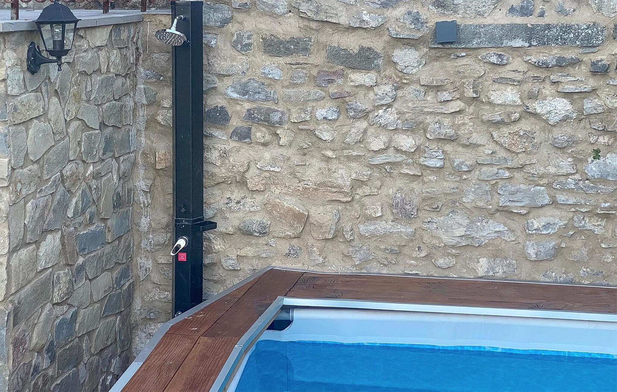 A stone wall with a pool, a black wall-mounted shower, and a wooden deck.