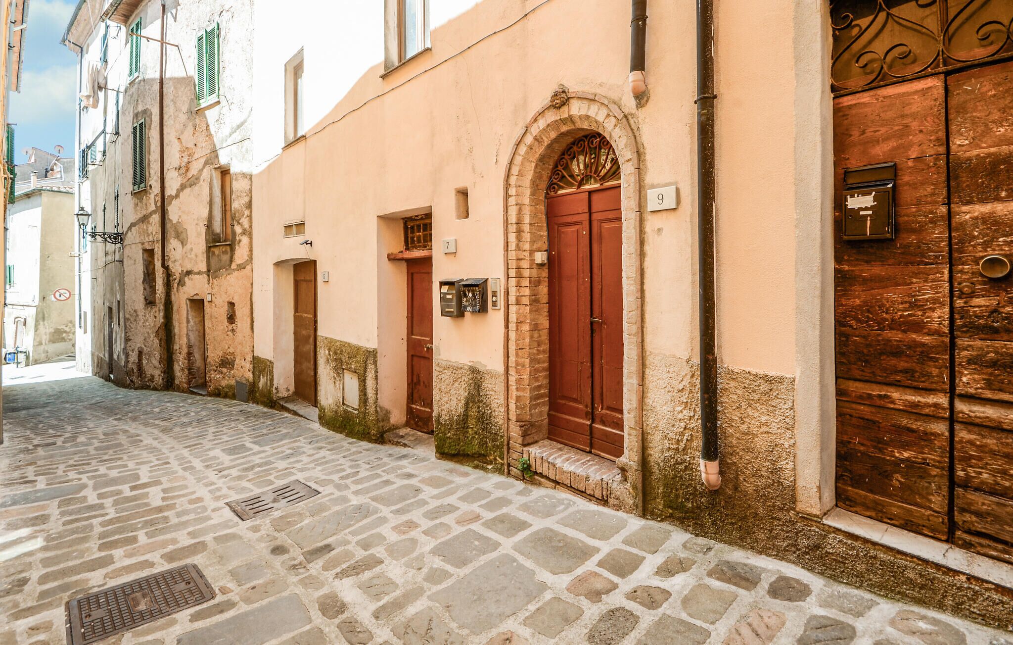 A narrow cobblestone street with buildings featuring arched doorways and numbered windows.