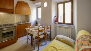 A compact kitchen with a gas stove, wooden cabinets, and a dining table set for four. - Gorgeous apartment in Monterotondo Marittimo (Monterotondo Marittimo)