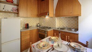 A kitchen with wooden cabinets, a gas stove, a sink, and a dining table set with plates and glasses. - Gorgeous apartment in Monterotondo Marittimo (Monterotondo Marittimo)