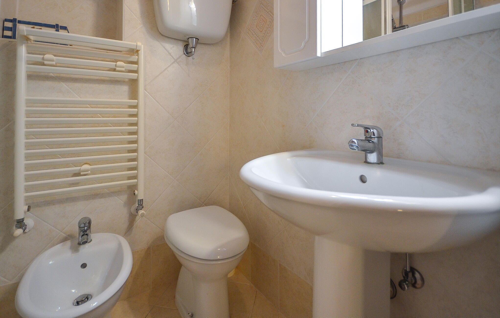 A bathroom with a pedestal sink, a toilet, and a towel rack.
