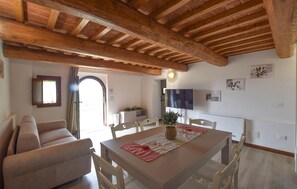 A dining area with a table, chairs, a sofa, a TV, and a wooden ceiling. - Il Borgo di Badia-L'Oliveta (Buti)