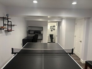 A room with a ping pong table, a desk with a chair, a TV, and a door with a coat rack. - Poolside Annapolis Retreat for Mid-Term Stays! (Annapolis)