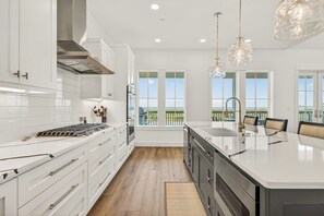 A modern kitchen with white cabinetry, a large island, and a view to the outdoors. - Multilevel beach house with water view, balconies, BBQ and private pool table (Port Aransas)