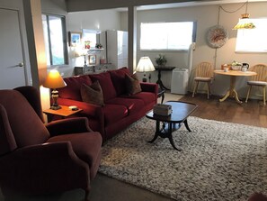 Un salon avec un canapé rouge, une table basse et une lampe. Il y a également un coin repas avec une table et des chaises.