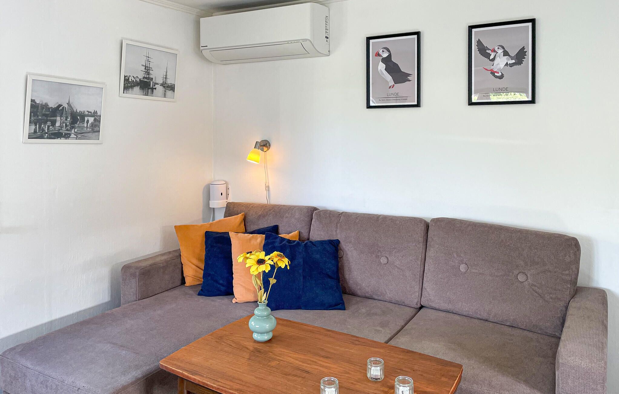 Ein Wohnzimmer mit grauem Sofa, einem Holztisch mit Vase und Kerzen sowie gerahmten Bildern an der Wand.