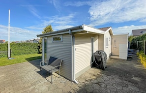 Ein kleines, eingeschossiges Haus mit einer Terrasse, einer überdachten Sitzgelegenheit im Freien und einer sichtbaren Garage.