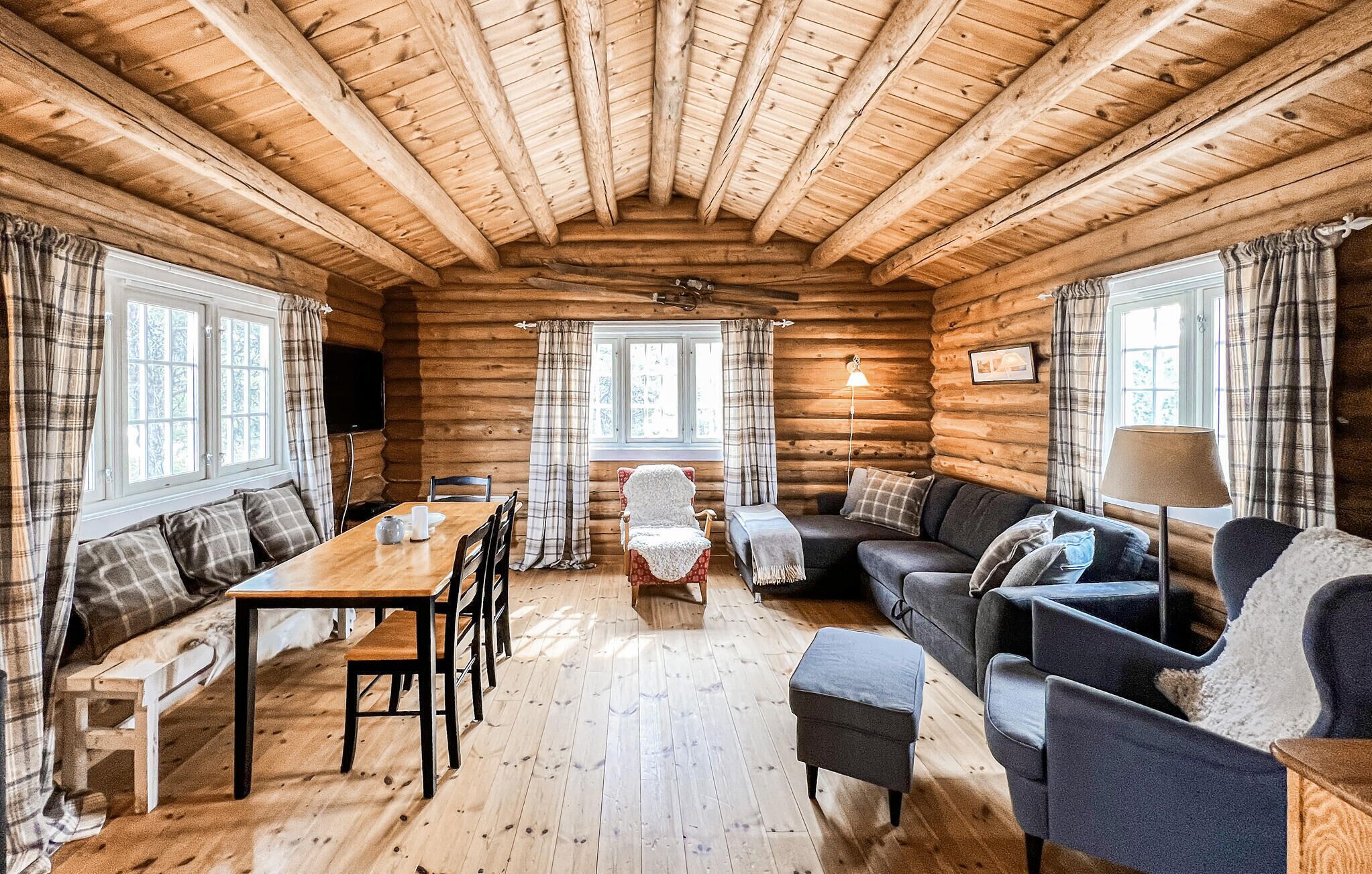 A log cabin interior with a wooden dining table, a sofa, a chair, and a lamp.