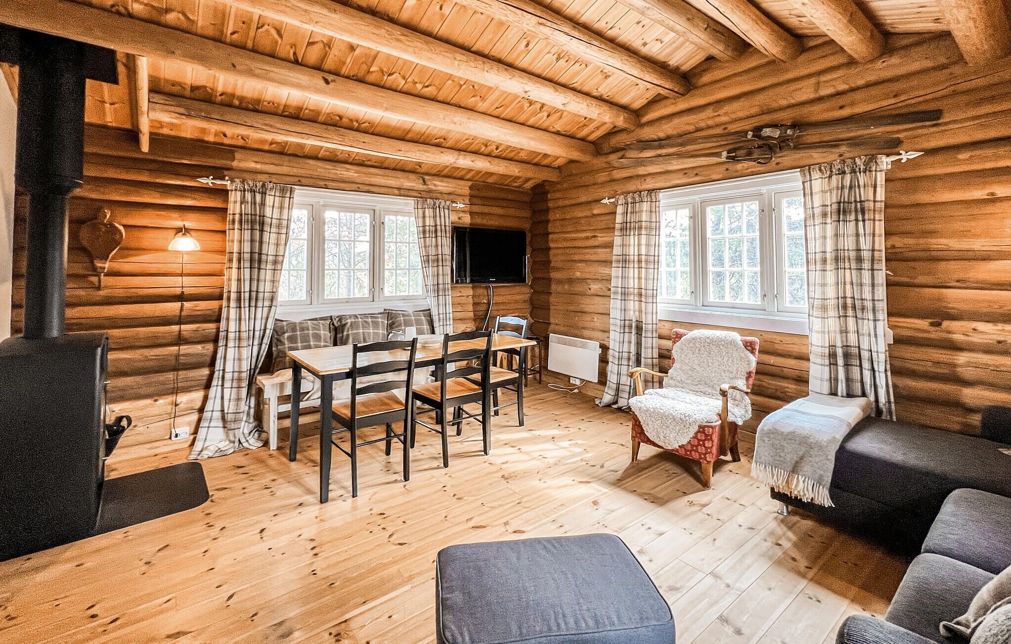 A log cabin interior with a wooden dining table, chairs, a sofa, and a television.