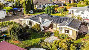 Ein Wohngebiet mit einem Haus, das eine überdachte Terrasse, einen umzäunten Garten und umliegendes Grün aufweist.