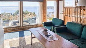 Een kamer met uitzicht op zee, een groene bank, een houten tafel en een raam met gordijnen.