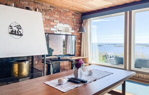 Eine Küche mit Backsteinwand, einem großen Fenster mit Meerblick, einem Tisch mit Blumenvase und einem Fernseher auf einem Schrank.