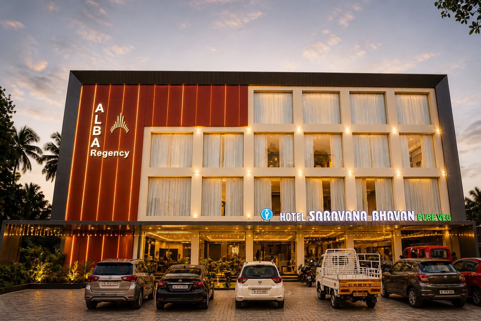A modern hotel with a prominent sign for 'ALBA Regency' and 'Hotel Saravana Bhavan Pure Veg'.