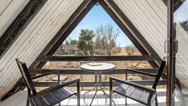 Une pièce triangulaire avec une table et des chaises, donnant sur des arbres et un bâtiment à l’extérieur.
