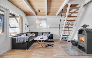 Ein modernes Wohnzimmer mit einer schwarzen Eckcouch, einem runden Couchtisch, einem Kamin, einer Holztreppe und einem Fenster mit Blick.