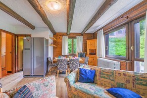 L’intérieur d’un chalet accueillant, avec un coin repas, une cuisine et un canapé agrémenté d’un coussin bleu.