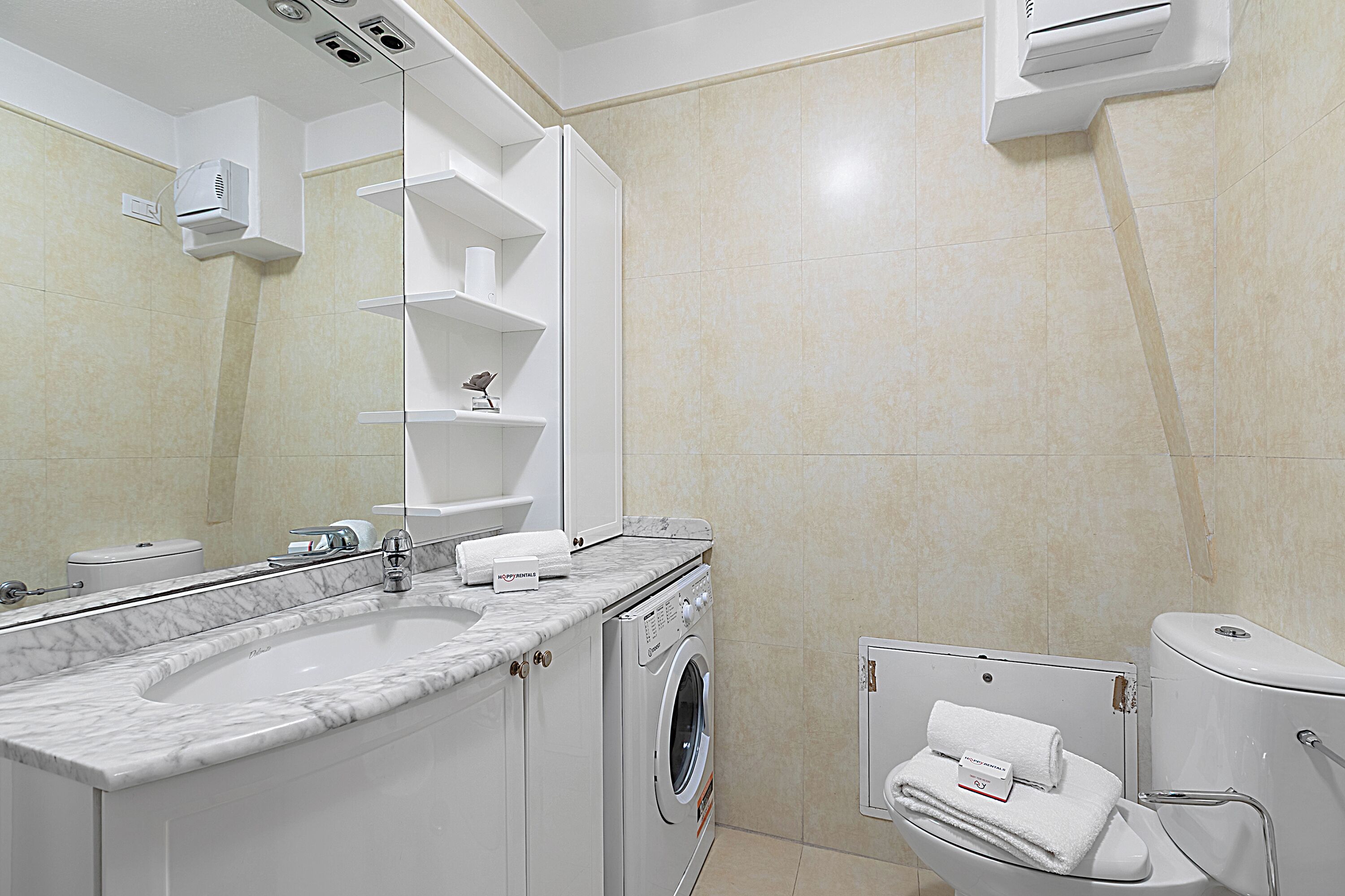 Un bany modern amb un lavabo de marbre, una rentadora, un vàter i un suport per a tovalloles.