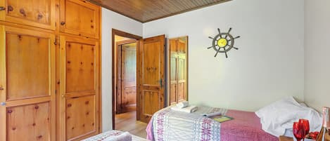 A bedroom with two beds, wooden wardrobes, a ship's wheel decoration, and a bottle of wine on a nightstand.
