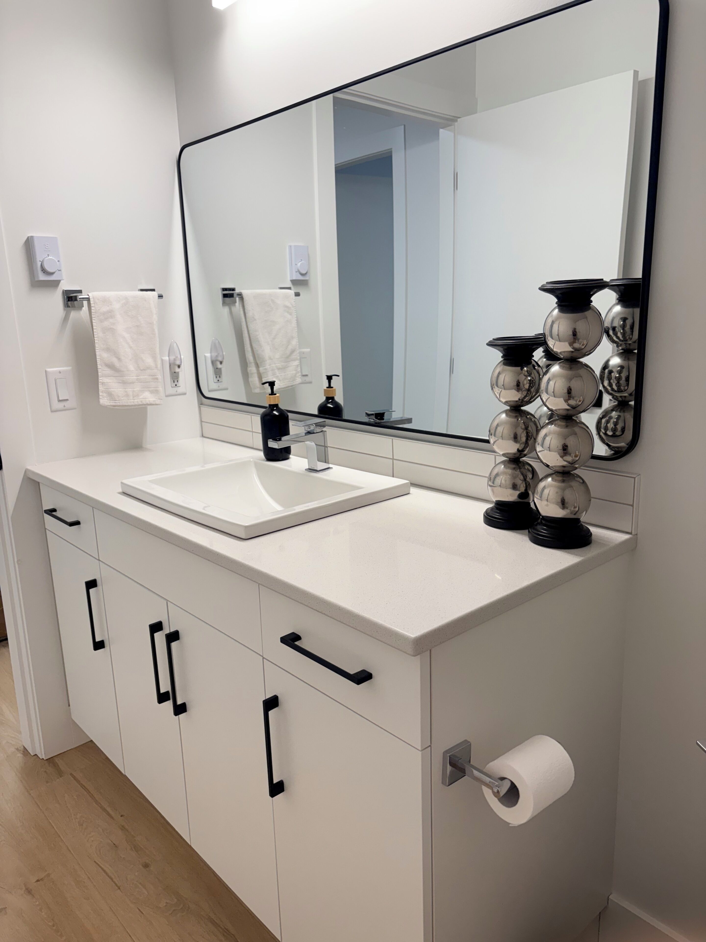 Un bagno moderno con un mobile lavabo bianco, uno specchio grande e un porta rotolo carta igienica.