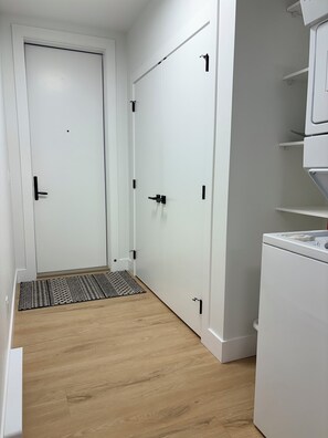 A hallway with a white door, a white cabinet, and a white appliance. - Upscale 1BR Suite in New Build | Nature Escape (Kelowna)