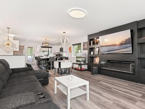 Ein modernes Wohnzimmer mit einem Ecksofa, einem weißen Couchtisch, einer Küchenzeile und einem großen, an der Wand befestigten Fernseher.