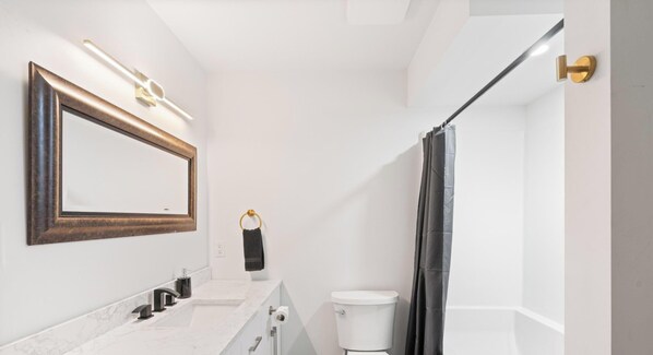 A modern bathroom with a marble sink, a toilet, a shower curtain, and a framed mirror. - Modern 5BR Home Near Lions Gate Glass Deck BBQ (West Vancouver)