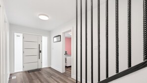 A hallway with a white door, a mirror, and a staircase with black rope handrails. - Modern 5BR Home Near Lions Gate Glass Deck BBQ (West Vancouver)