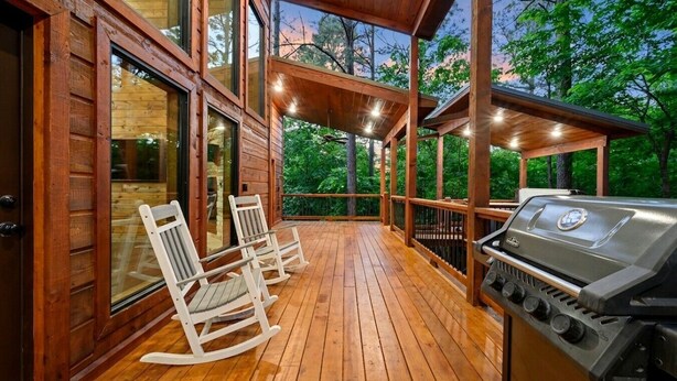 Une terrasse en bois équipée d’un barbecue, de deux fauteuils à bascule et d’une porte vitrée donnant sur un espace intérieur.