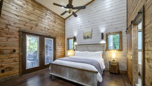 Une chambre à coucher avec un lit, des murs en bois, un ventilateur de plafond et deux fenêtres.