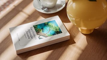 A book, a cup of coffee, and a vase with flowers on a wooden table.