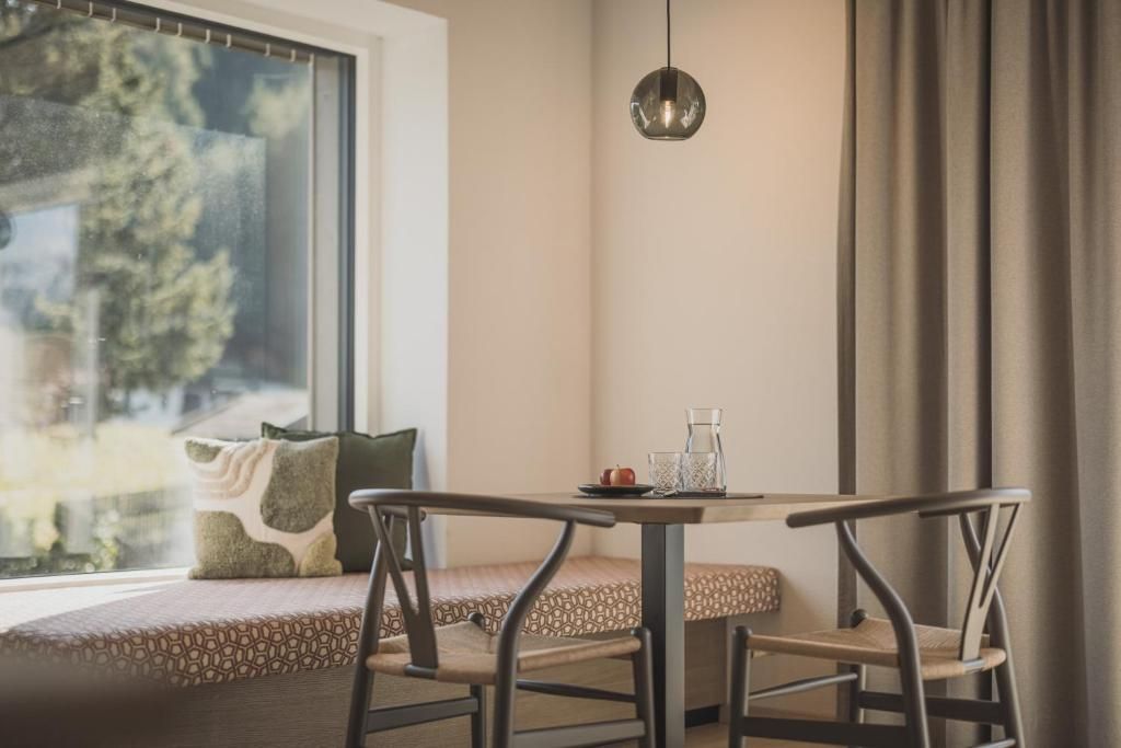 A cozy seating area with a table and chairs, a window with a view of trees, and a pendant light.