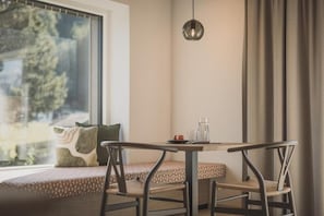 A cozy seating area with a table and chairs, a window with a view of trees, and a pendant light. - SOLU Apartments (Seefeld)