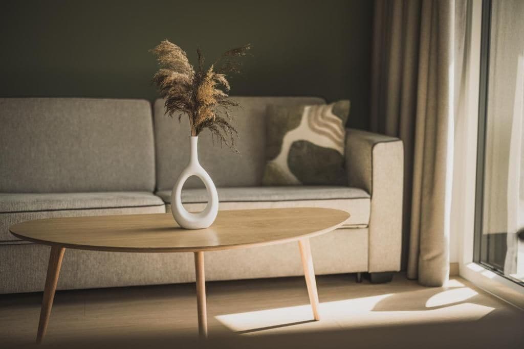 A modern living room with a sofa, a round coffee table, and a vase with dried plants.