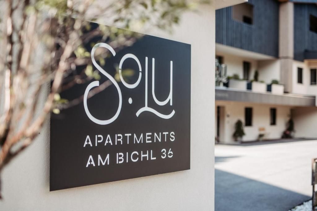 Une enseigne indiquant « Solu Apartments », avec un immeuble moderne en arrière-plan.