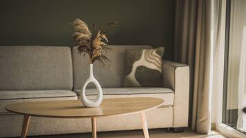 A modern living room with a round wooden coffee table, a white vase with dried plants, a grey sofa, and a patterned throw pillow.