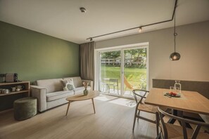 A modern living room with a sofa, a dining table, and a large sliding glass door leading to a garden. - SOLU Apartments (Seefeld)
