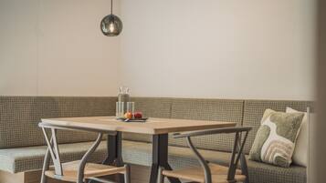 Un comedor con una mesa, sillas y un banco. Un frasco y frutas están sobre la mesa.