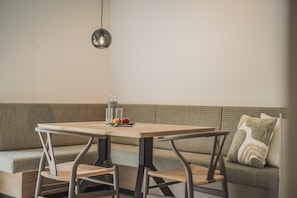 Un comedor con una mesa, sillas y un banco. Un frasco y frutas están sobre la mesa.