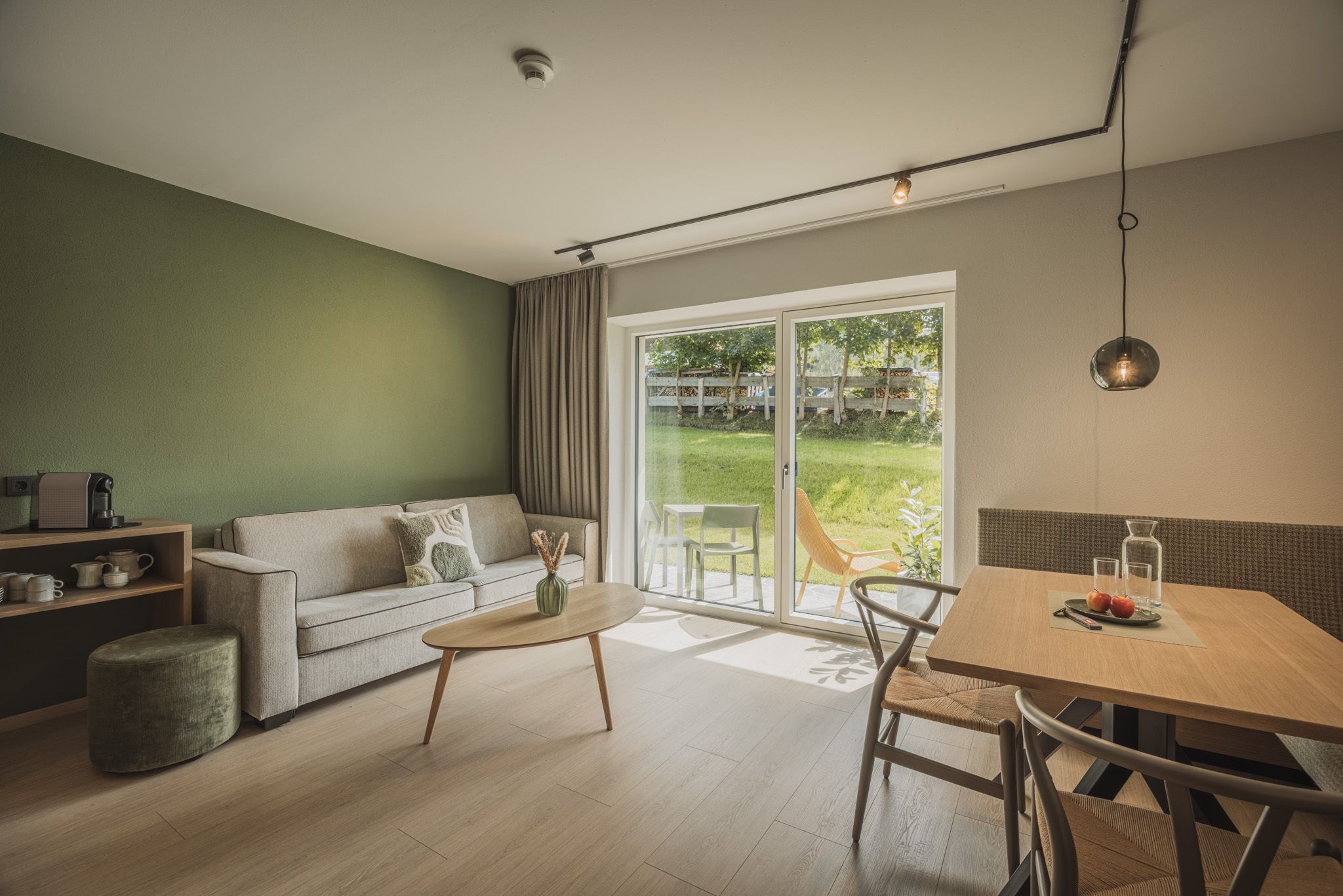 Un salon moderne avec un canapé, une table basse et une table à manger. Une porte-fenêtre coulissante donne accès à un balcon aménagé avec des sièges d’extérieur.