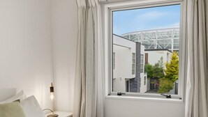 Ett sovrum med ett fönster, en sänglampa och utsikt över en byggnad med en fasad av glas.