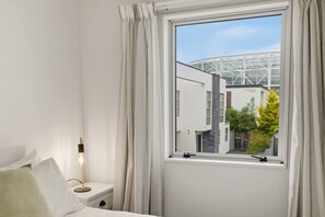 Ein Schlafzimmer mit Fenster, Nachttischlampe und Blick auf ein Gebäude mit Glasfassade.