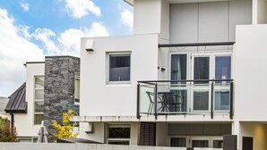 En modern bostadsbyggnad i två våningar med en balkong, stora fönster och en accentvägg i sten.