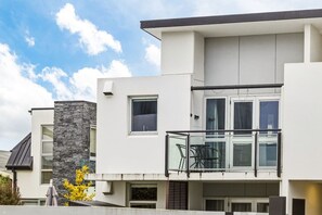 Ein modernes Wohnhaus mit zwei Stockwerken, einem Balkon, großen Fenstern und einer Wand aus Naturstein.
