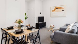 Ett modernt vardagsrum med en matplats, en grå soffa, en tv och en tavla på väggen.