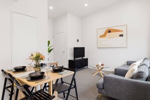 Ein modernes Wohnzimmer mit Essbereich, einem grauen Sofa, einem Fernseher und einem Gemälde an der Wand.