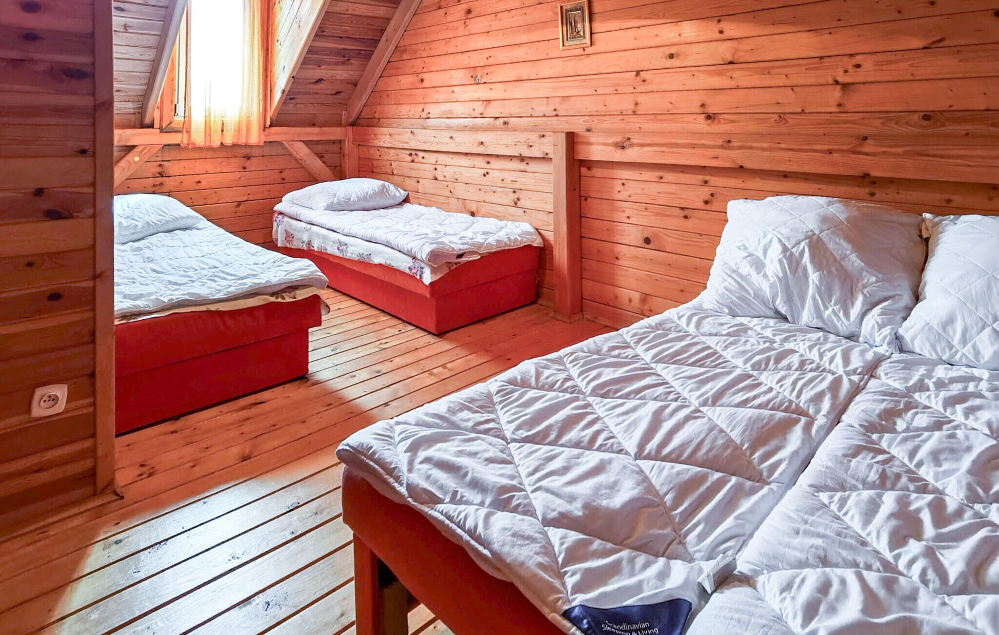 Eine Holzhütte mit Schlafzimmer im Loft-Stil, inklusive zwei Betten, einer roten Bank und einer Holzzahlende.